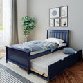 Navy blue wooden twin bed with pull-out trundle, blue striped duvet and pillow in a modern kids bedroom with hardwood floor, potted plant, framed sports wall art and natural light