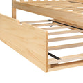 Close-up of a light pine wooden platform bed frame with slatted bed base, under-bed trundle rails with small caster wheel and black metal support straps in a natural wood finish