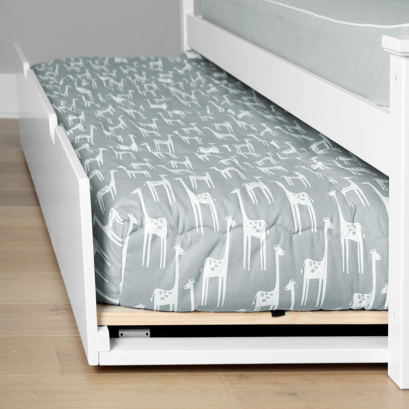 White wooden trundle bed with giraffe-patterned bedding on light wood floor.