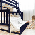Navy blue wooden bunk bed with pull-out trundle, ladder and safety rails in bright kids' bedroom with white bedding and plush toys
