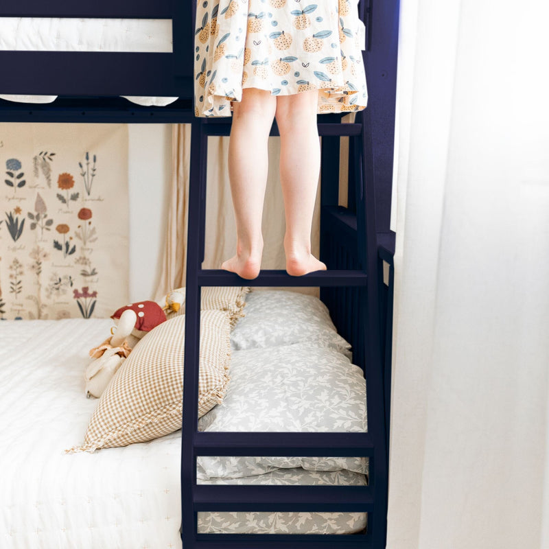 Child climbing a bunk bed ladder in a cozy bedroom with decorative pillows and floral bedding.