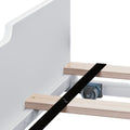 Close-up of white bed frame with wooden slats, black support strap and metal caster wheel