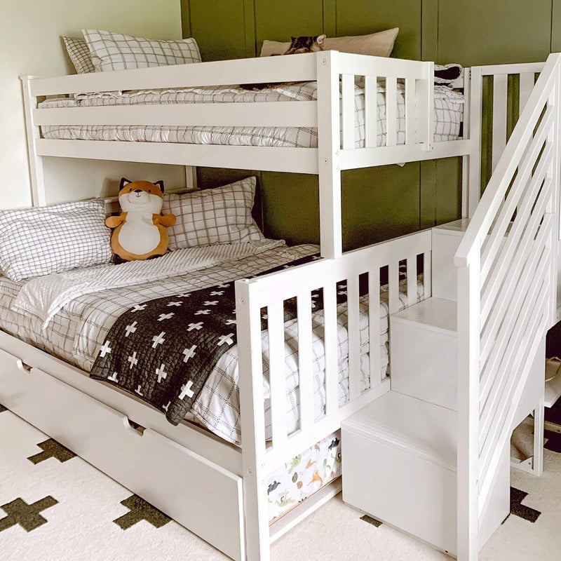 White wooden L-shaped bunk bed with built-in stairs, gray plaid bedding, black cross quilt, fox plush toy, green accent wall and under-bed storage in a modern kids' bedroom