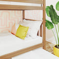 Wooden bunk bed with white bedding and yellow pom-pom pillow against pink geometric wallpaper and banana-leaf plant
