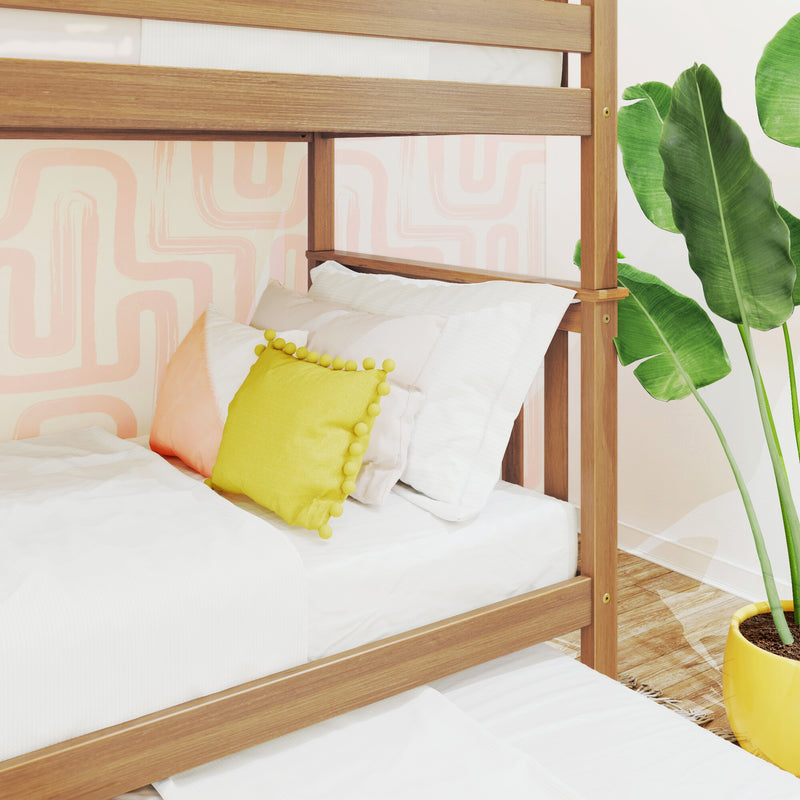 Wooden bunk bed with white bedding and yellow pom-pom pillow against pink geometric wallpaper and banana-leaf plant