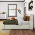 Modern kids bedroom with a stuffed fox on green striped bedding, cream upholstered bed, orange accent pillows, "Oliver" pennant on wall, abstract dinosaur artwork, white dresser with colorful books and gray-trimmed windows