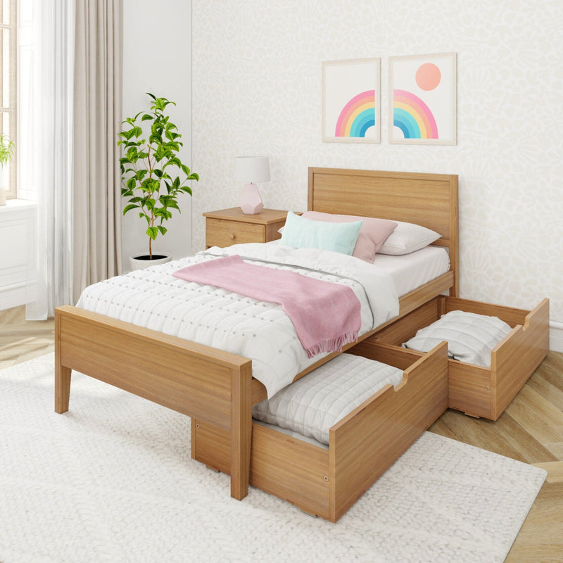 Wooden twin storage bed with two pull-out drawers, white quilt and pink throw in a bright modern bedroom with bedside table, lamp, potted plant and rainbow wall art