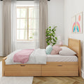 Sunlit minimalist bedroom with oak storage bed, white and pastel bedding, pink throw, potted green plant and rainbow wall art