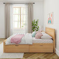 Scandinavian bedroom with oak storage bed, white quilt, pink throw and pastel pillows, sheer curtains, potted plant and rainbow wall art by a sunlit window