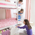 Three girls playing on a white bunk bed with pink bedding, ladder and under-bed storage drawer in a bright kids' bedroom