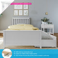 White wooden single bed with pull-out trundle storage, yellow polka-dot duvet and slats, white bedside table with vase and books, botanical wall art and gold pendant light — features countersunk color-matched hardware, 100% New Zealand pine frame and 400 lb support bar