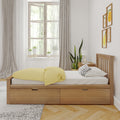 Scandinavian bedroom with wooden bed, yellow duvet, polka-dot pillow, indoor plants, large window and neutral curtains.