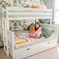 Cozy children's bedroom with white bunk bed and under-bed drawers, striped bedding, colorful floral wallpaper and throw pillows, child sitting on lower bunk holding a pink cushion by a sunlit window