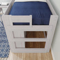 Top-down view of a whitewashed wooden loft bed with navy blue fitted sheet, safety rail, hardwood floor and blue patterned rug
