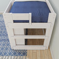 Top-down view of a white wooden twin loft bed with navy blue fitted sheet, blue geometric area rug and hardwood floor in a modern kids' bedroom