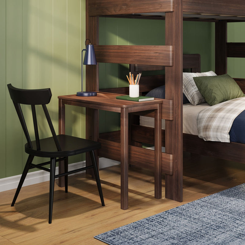 Wooden bunk bed with built‑in desk and navy lamp, study nook with black chair, pencil holder and plaid bedding against green paneled wall on hardwood floor