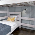 Whitewashed wooden bunk bed in modern kids' bedroom with gray paneled wall, blue quilt, patterned yellow pillow, wall-mounted reading lamp and dark hardwood floor