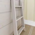 Close-up of a light wood ladder leaning against whitewashed wood-paneled wall in a bright neutral interior, showing ladder rungs, visible screw hardware and woven jute rug, ideal for modern coastal bedroom decor