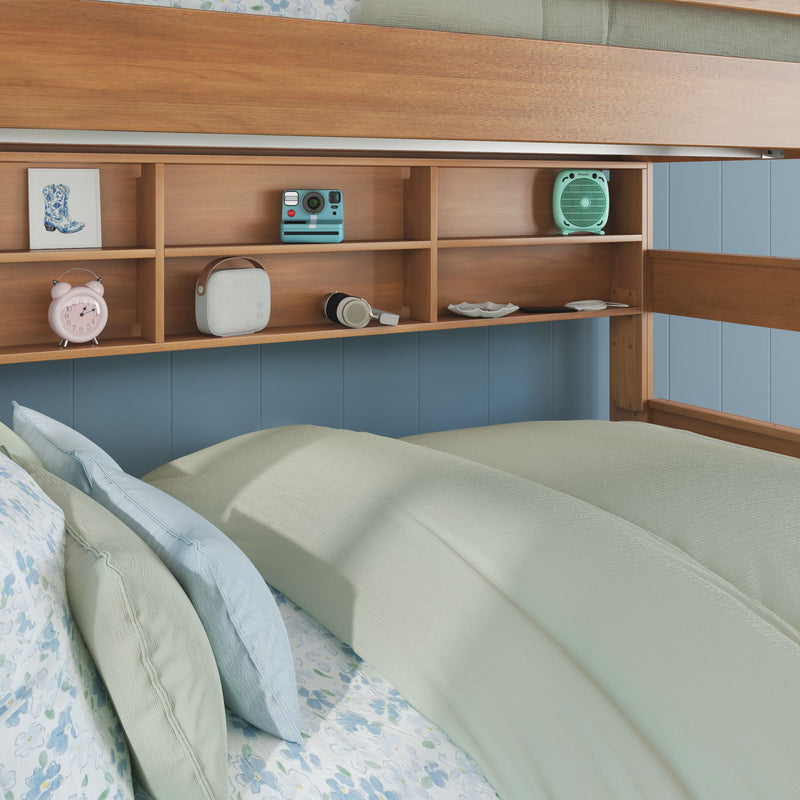 Bunk bed with built-in wooden shelving displaying retro alarm clock, instant camera, portable speaker and mint fan above floral pastel bedding and blue paneled wall