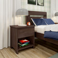 Modern walnut nightstand with white table lamp, red alarm clock and stacked books beside a wooden bed with navy blue pillows and white linens in a cozy bedroom interior
