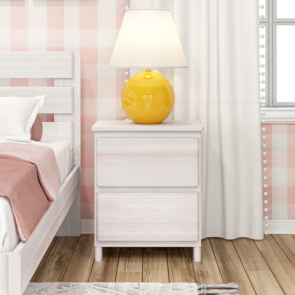 Nightstand with white wood finish featuring a vibrant yellow lamp, next to a bed with pink bedding and checkered wallpaper.