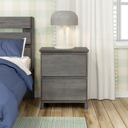 Gray wooden nightstand with lamp and bed in cozy bedroom setting.