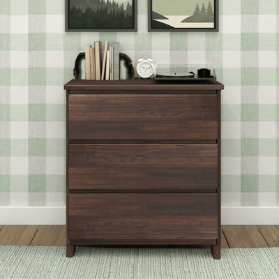 Dark walnut three-drawer dresser with books, geode bookends, alarm clock and record player against green plaid wall with framed nature prints