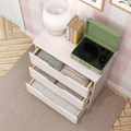 Top-down view of pastel pink dresser with open drawers of folded blankets, green portable record player, lamp and books in a nursery room