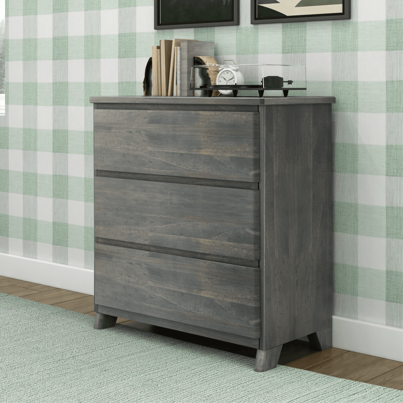 Gray wooden dresser with three drawers in a modern bedroom featuring green checkered wallpaper and a light green carpet.