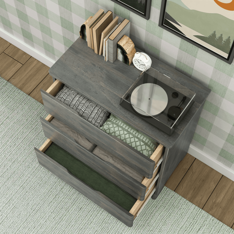 Modern wooden dresser with open drawers, displaying neatly folded blankets and books on top, set in a chic home interior with wooden flooring.