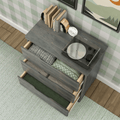 Gray wooden three-drawer dresser with open drawers showing folded blankets and linens, vintage turntable and books on top, white alarm clock, green plaid wallpaper, hardwood floor and green area rug — cozy bedroom storage and organization