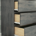 Close-up of modern gray wood dresser with three partially open drawers revealing natural wood interiors, white metal drawer slides and wood grain finish