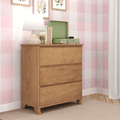 Natural wood three-drawer dresser in pink gingham nursery with white table lamp, green record player, children's books and botanical wall art