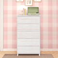 White wooden five-drawer dresser in a cozy nursery with pink gingham wallpaper, lamp, books and a green record player on top