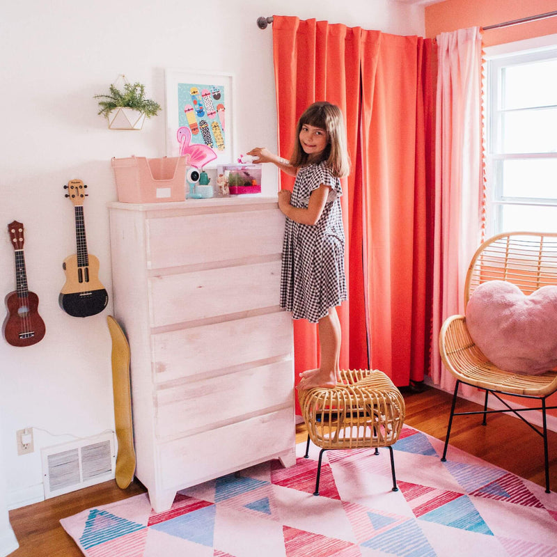 Child standing on chair reaching for dresser in colorful bedroom with musical instruments and bright curtains.