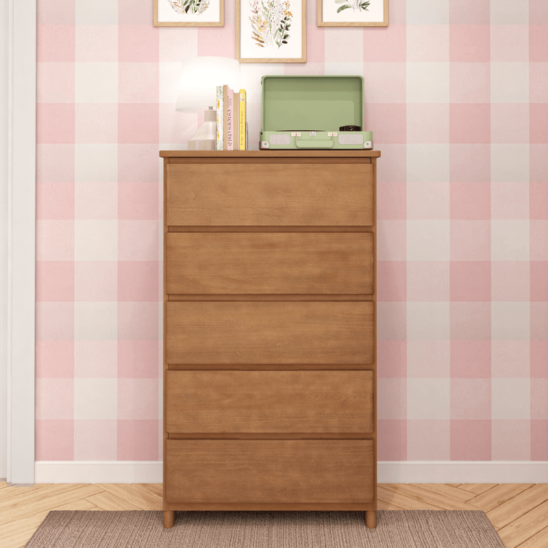Tall mid-century modern five-drawer wooden dresser with a green record player, books and table lamp on top against pink checkered (gingham) wallpaper in a cozy bedroom with herringbone hardwood floor and rug