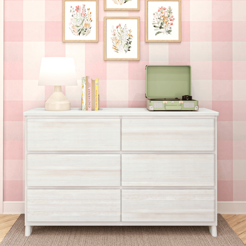 White dresser in pastel pink gingham nursery with lamp, children's books, green record player and framed floral prints — kids' room decor