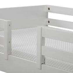 Close-up of a white wooden toddler bed with safety guard rails and a quilted white mattress