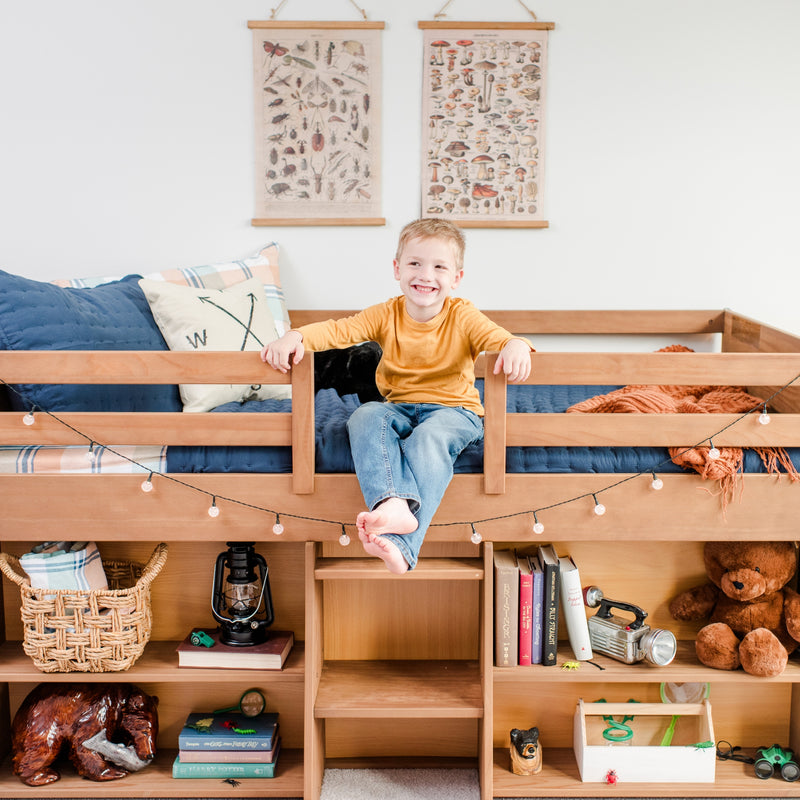 Child sitting on a wooden loft bed with storage shelves, surrounded by toys and books in a cozy bedroom.