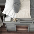 Top view of gray wooden toddler bed with built-in shelf holding a striped plush elephant toy and book, white and gray pillows and beige blanket on hardwood floor
