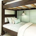 Close-up of dark wood bunk bed frame and slats with mint green pillows, quilted bedding, and white wall sconce in a modern bedroom
