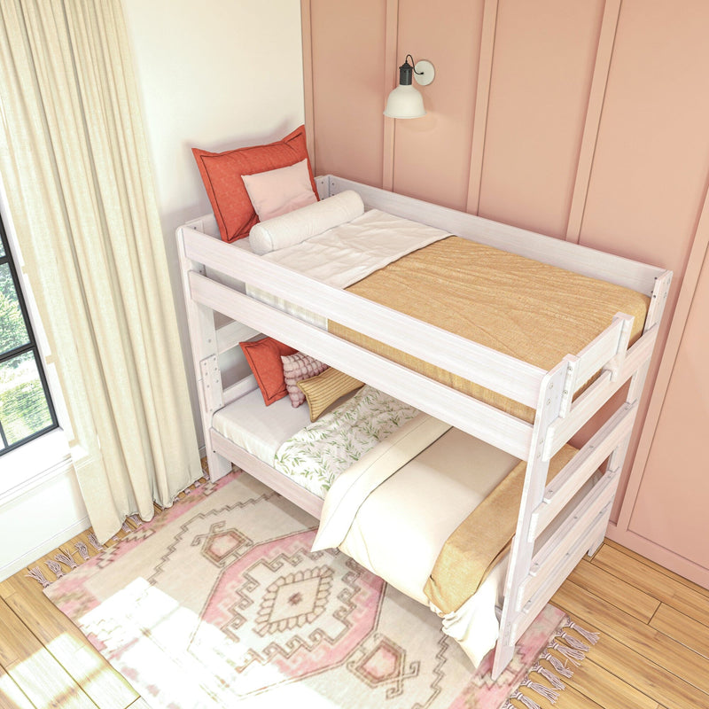 White wooden bunk bed with cozy bedding and decorative pillows against a peach-colored wall, featuring a soft, patterned area rug on hardwood flooring.