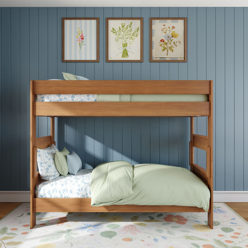 Wooden bunk bed with pastel green bedding and floral sheets against a blue vertical paneled wall, three framed floral prints above and floral rug in a cozy kids' bedroom