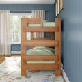 Natural wood bunk bed in kids' bedroom with green bedding, blue vertical shiplap walls, sheer curtains, large window, floral area rug and framed artwork