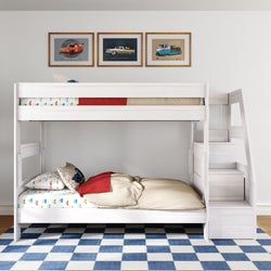 White wooden twin-over-twin bunk bed with side staircase and storage in a children's bedroom, car-themed bedding and framed vintage car wall art above, on a blue and white checkered rug