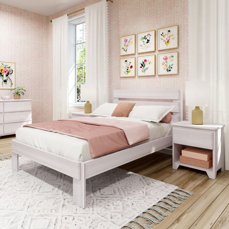 White wood platform bed with blush pink bedding in a modern feminine bedroom, matching nightstands and lamps, floral gallery wall, white patterned rug, and natural light from a large window