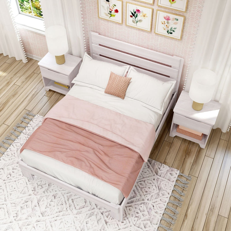 Top-down view of a cozy modern feminine bedroom with white wooden bed frame, blush pink duvet and throw, matching nightstands with lamps, floral wall art and patterned boho rug on hardwood floor