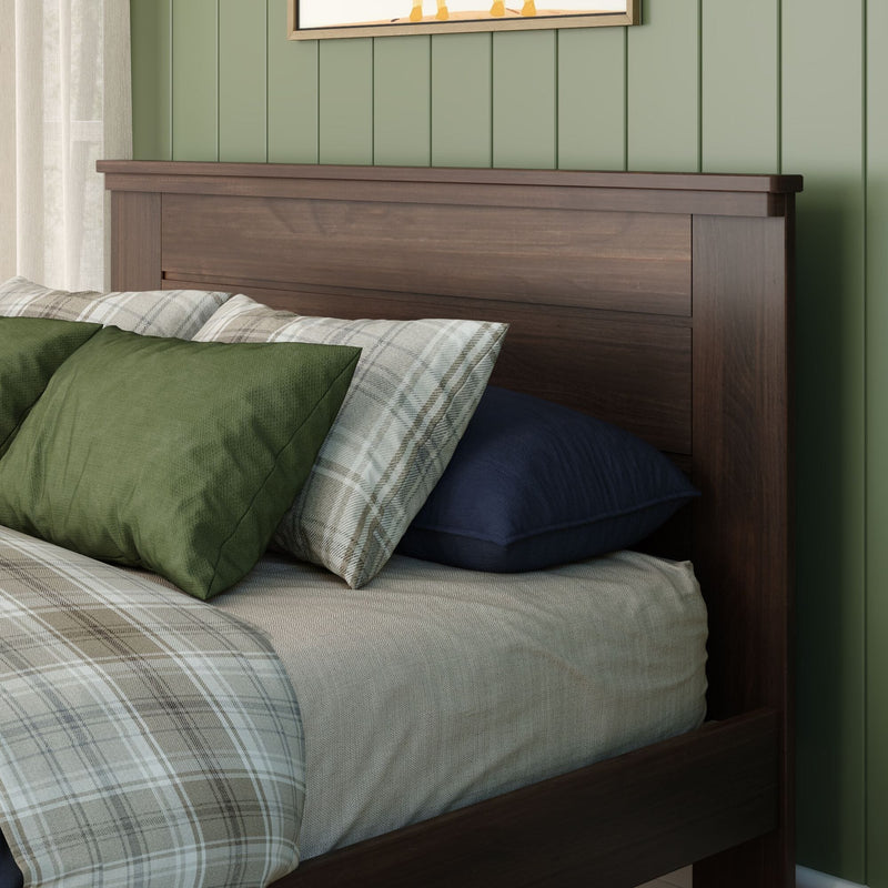 Dark wood headboard with green pillows and plaid bedding against a green paneled accent wall in a cozy bedroom interior
