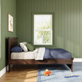 Kids bedroom with green vertical shiplap walls, dark wood bed, plaid and green pillows, sunlit window and wooden toy cart on blue rug