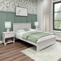 Modern bedroom with sage green board-and-batten accent wall, whitewashed wooden bed and nightstands, light green quilt and pillows, botanical wallpaper, bedside lamps, large window, hardwood floors and patterned area rug